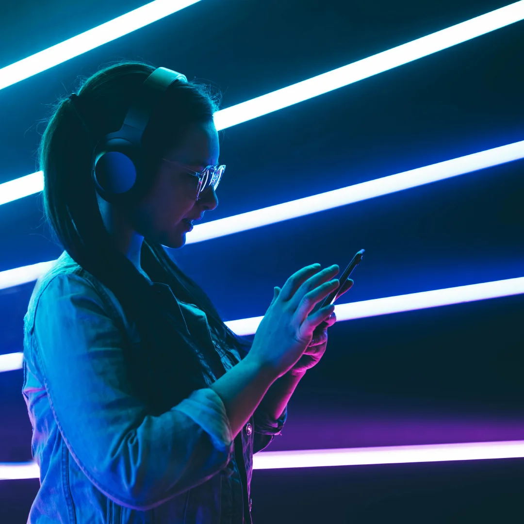 Mujer con auriculares y teléfono frente a luces de neón.